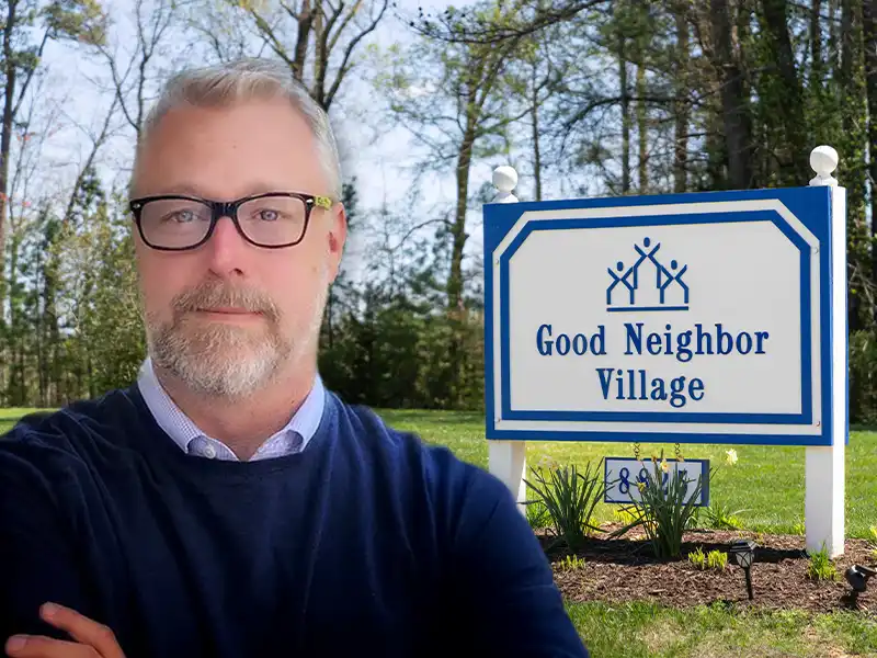 Ryan Corrigan standing in front of the Good Neighbor Village sign.