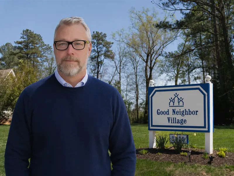 Ryan Corrigan standing outside Good Neighbor Village next to the organization's entrance sign.